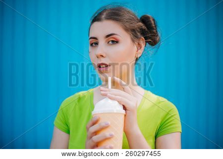 Portrait Of A Girl Against A Bright Blue Wall. Emotional Girl Holding A Plastic Glass With A Refresh