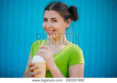 Portrait Of A Girl Against A Bright Blue Wall. Emotional Girl Holding A Plastic Glass With A Refresh
