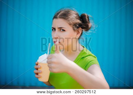 Portrait Of A Girl Against A Bright Blue Wall. Emotional Girl Holding A Plastic Glass With A Refresh