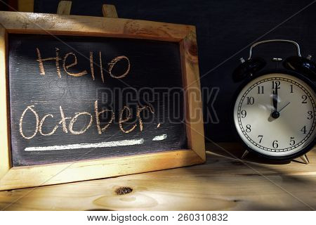 Hello October. Back To School Concept. Alarm Clock On Wooden With Blackboard On Background
