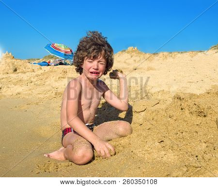 Crying Boy On The Beach. A Small Child Sitting By The Sea And Hysterically Crying