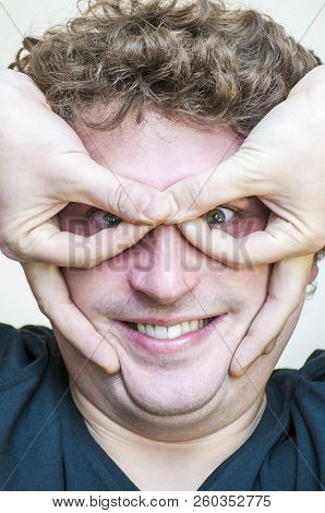 Portrait Of Young Caucasian Ethnicity Funny Playful Curly Man Shows Imaginary Eyeglasses With Finger
