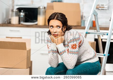 Sad Beautiful Woman Sitting On Laddder In Kitchen With Cardboard Boxes During Relocation At New Home