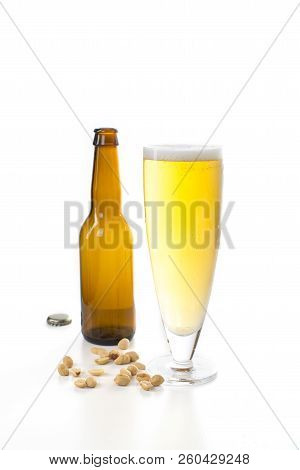 One Brown Beer Bottle And A Glass Of Beer, Set Against A White Background And Some Beer Nuts At The 