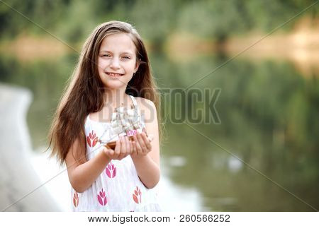 girl playing with a toy sailing ship by the river