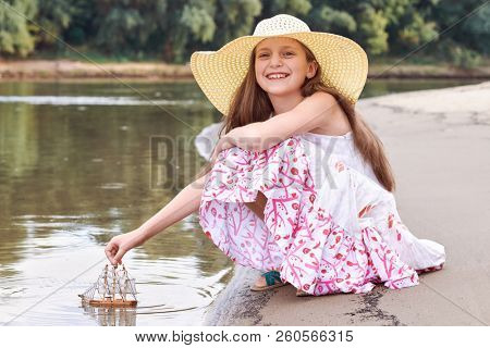 girl playing with a toy sailing ship by the river