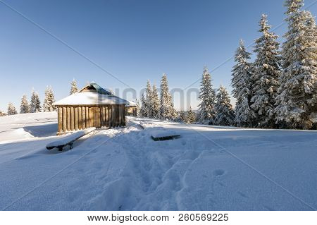 Fairy Tale Beautiful Winter Sunny Landscape. Wooden Shepherd Hut On Mountain Snowy Clearing Among Ta