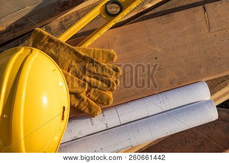 Abstract of Constrcution Hard Hat, Gloves, Level and House Plans Resting on Wood Planks.