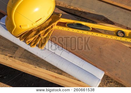 Abstract of Constrcution Hard Hat, Gloves, Level and House Plans Resting on Wood Planks.