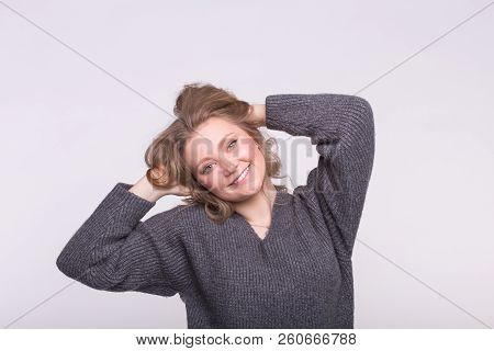 Young Blonde Woman With Hand In Hair Wearing Gray Sweater On White Background