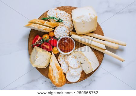 Cheese Board With Tomatoes, Jam, Baguette, Bread Sticks And Crackers On Marble Background, Top View