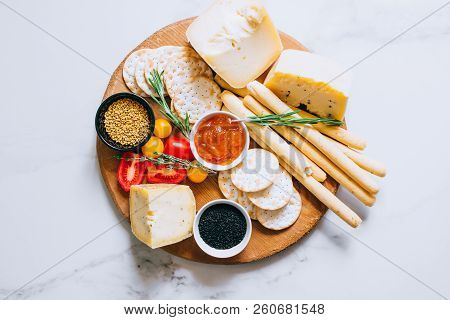 Cheese Board With Tomatoes, Jam, Baguette, Bread Sticks And Crackers On Marble Background, Top View