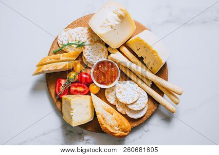 Cheese Board With Tomatoes, Jam, Baguette, Bread Sticks And Crackers On Marble Background, Top View