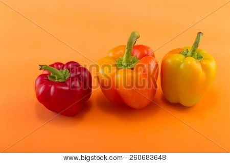 Sweet Bellpepper. Two Orange-yellow And One Red Sweet Bellpeppers On An Orange Background. Three Pie