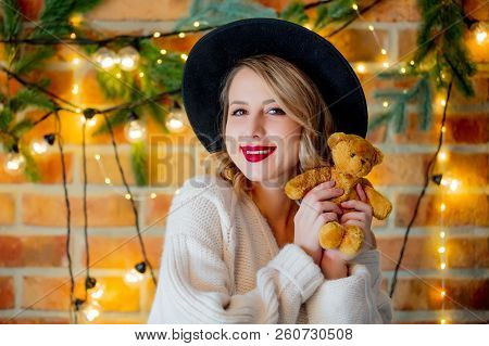 Portrait Of A Young Cozy Woman In White Sweater With Teddy Beartoy And Christmas Lights On Backgroun