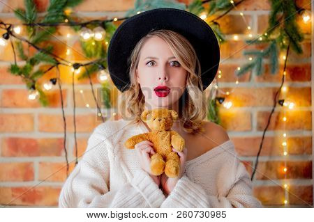 Portrait Of A Young Cozy Woman In White Sweater With Teddy Beartoy And Christmas Lights On Backgroun