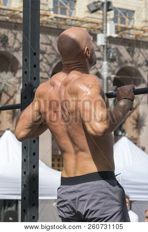 Athlete Muscular Fitness Male Model Pulling Up On Horizontal Bar In A Gym. Closeup Of Strong Athlete
