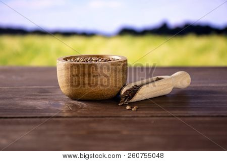 Lot Of Whole Fresh Brown Flaxseeds In A Scoop With Wooden Bowl With Green Wheat Field In Background