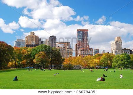 New York City Manhattan skyline panorama viewed from Central Park with cloud and blue sky and people in lawn.