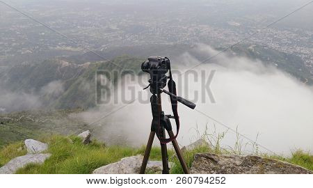 Camera On A Tripod In The Background Of A Valley Above The Clouds