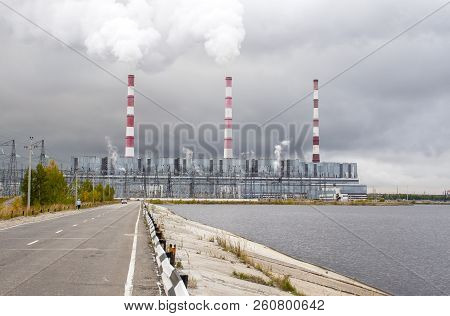 Thermal Power Plant With Bright Chimneys In Cloudy Weather Against The Background Of A Cloudy Sky.
