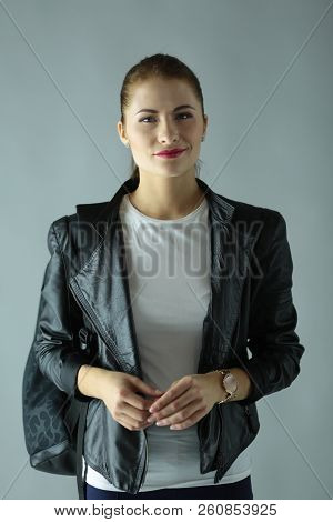 Portrait Of Beautiful Young Brunette Woman In Stylish Black Jacket On Gray.