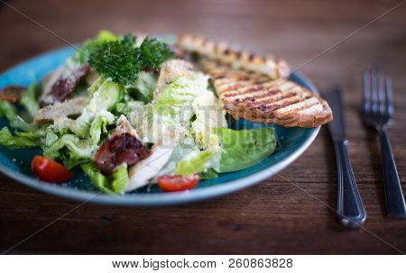 Fresh Caesar Salad In Blue Plate On Dark Wooden Table With Cuttlery Aside