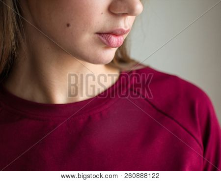 Fashion photo of a beautiful smiling brunette woman in a red sweater posing over gray empty background.