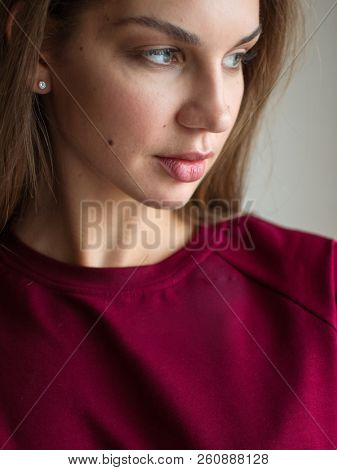 Fashion photo of a beautiful smiling brunette woman in a red sweater posing over gray empty background.