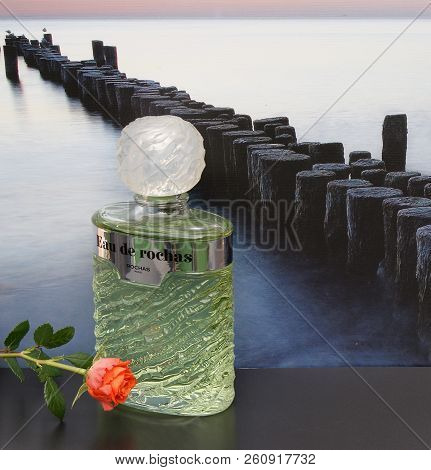 Eau De Rochas, Fragrance For Ladies, Large Perfume Bottle In Front Of The Picture Of A Groyne In The