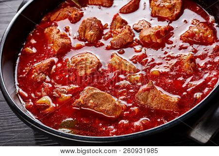 Close-up Of Hearty Red Chile And Pork Stew Or Carne Adobada In A Dutch Oven On A Black Wooden Table,