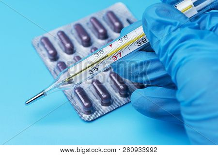 Hand In Glove Holding A Thermometer Of The Health Of Medicine On A Blue Background.