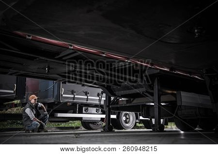 Caucasian Trucker In His 30s Checking On Truck Trailers Undercarriage. Transportation Industry Theme
