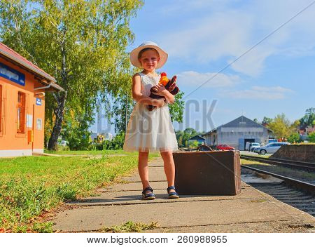 Cute Girl Holding Stuffed Animal On A Railway Station, Waiting For The Train With Vintage Suitcase. 