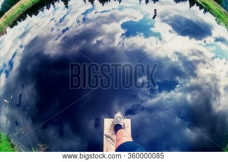 Deceptive Reflection Of Blue Sky With Clouds On Ponds Water. Mans Foot Steps Above Water As If He Is