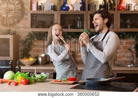 Father And Daughter Having Fun While Preparing Lunch In Kitchen, Singing Loud, Using Spatula And Bro