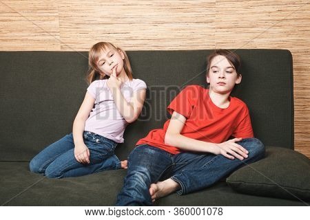Frustrated siblings sittng on sofa stuck at home being in self-isolation. Quarantine and lockdown protective measures against spreading of coronavirus pandemic disease