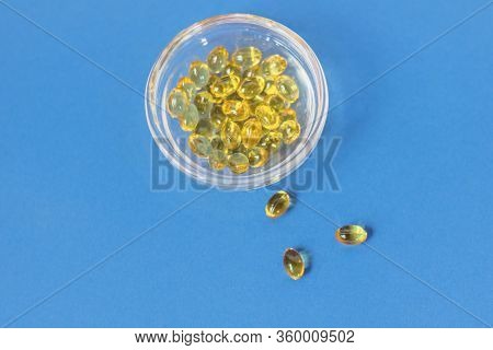 Yellow Gelatin Capsules With Vitamin D3 In A Glass Container On A Blue Background. Pharmaceutical Th