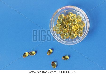 Yellow Gelatin Capsules With Vitamin D3 In A Glass Container On A Blue Background. Pharmaceutical Th