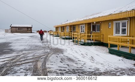 Unrecognized Man Walking On A Snowy Road To The Yellow Winter Cottage House In Iceland