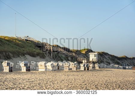 German Beach Resort With Wicker Chairs, Dunes Covered In Tall Grass In Morning Sunlight, On Sylt Isl