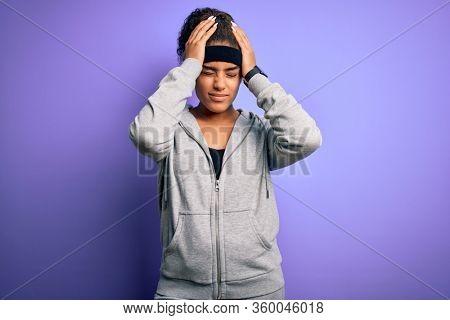 Young african american sportswoman doing sport wearing sportswear over purple background suffering from headache desperate and stressed because pain and migraine. Hands on head.
