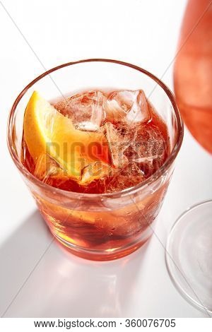 Negroni cocktail close up. Alcohol strong aperitif drink in glass side view. Beverage with red vermouth, Campari liqueur, gin, orange and ice in drinkware. Italian cocktail portion in glassware