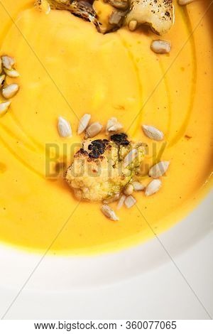 Pumpkin soup in white bowl. Served main course close up. Vegetable cream soup decorated with seeds. Restaurant food portion, main course. Vegetarian supper. Dinner, gourmet meal in plate