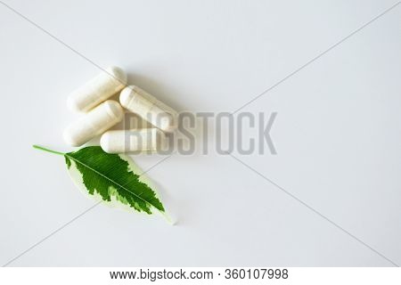 Pill Capsules Heap And Plant Leaf On White Background With Copy Space, Top View. Concept Alternative