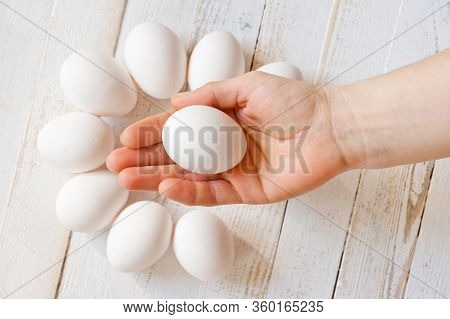 A White Chicken Egg Lying In A Man’s Hand, Shot On A White Painted Wooden Surface. Background For Li