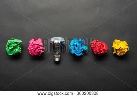 Lightbulb And Crumpled Colorful Paper Balls On Black Background. Successful Solution Of Problem. Ide