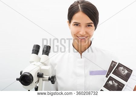 Portrait Of A Mixed Race Gynecologist Sitting In An Office Near A Colposcope. Gynecologist Professio