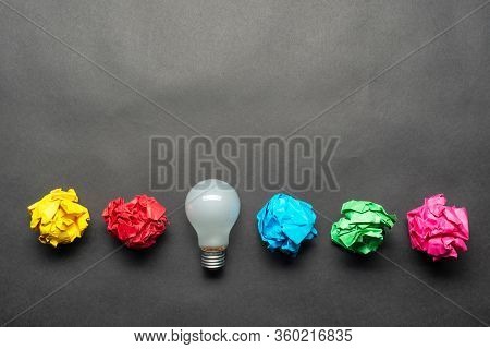 Lightbulb And Crumpled Colorful Paper Balls On Black Background. Successful Solution Of Problem. Ide