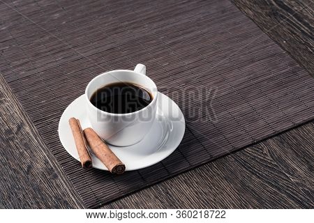 Cup Of Black Coffee On Table. Top View White Cup And Cinnamon Sticks On Porcelain Saucer. Close Up F